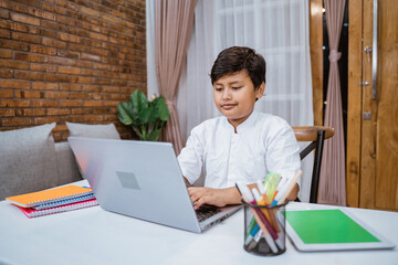 Cheerful boy writing using laptop while doing schoolwork at home