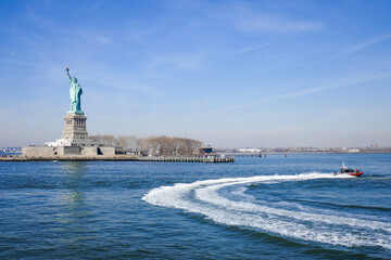 Statue of Liberty in NY Harbor with racing US Coast Guard Patrol Boat, blue sky and water