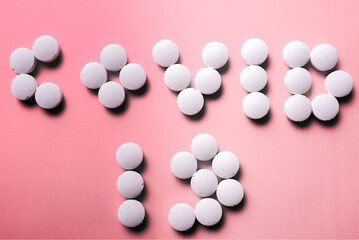 COVID 19 lettering made of white medical pills on a bright pink background