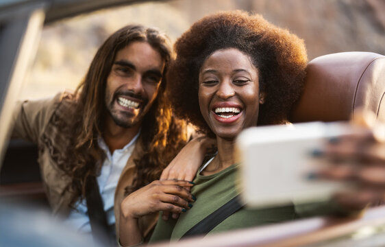 Happy young couple taking selfie with mobile smartphone while doing road trip - Travel people having fun driving in convertible car discovering new places - Relationship and vacation lifestyle concept