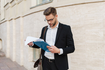 Handsome unshaven businessman posing with clipboard on city street