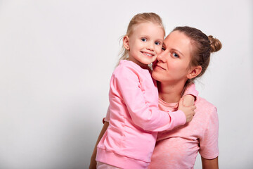 Little daughter hugging and kissing her mother spending time together in pink clothes over gray background. Mother's Day love family, parenthood childhood concept