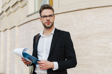 Handsome unshaven businessman posing with clipboard on city street