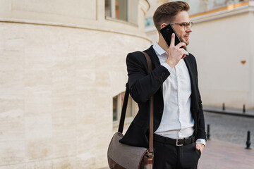 Handsome unshaven businessman in eyeglasses talking on mobile phone