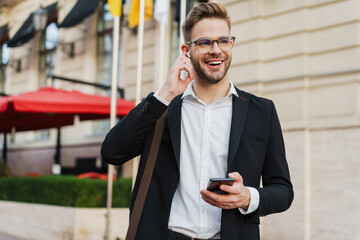 Handsome joyful businessman using wireless earphone and mobile phone