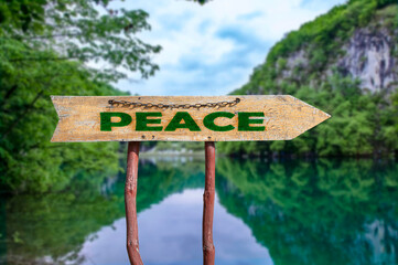 Peace wooden arrow road sign against lake and forest background.
