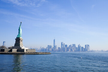 Obraz premium Statue of Liberty in NY Harbor on bright sunny day with blue sky and Manhattan in the distance