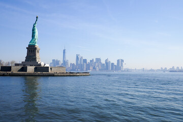 Statue of Liberty in NY Harbor on bright sunny day with blue sky and Manhattan in the distance - obrazy, fototapety, plakaty