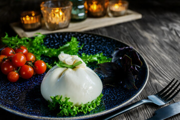 Traditional Italian dish of burrata Stratocell. Burrata on a dark plate is served for a romantic dinner with tomatoes and arugula