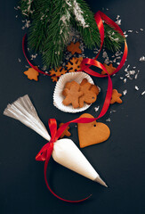 Christmas gingerbread cookies with fir festive decoration with snow and pastry bag with icing on black background, view from above. Holiday food, homemade baking, Christmas and New Year traditions. - 385777650