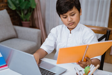 a boy doing homework at home with laptop and writing notes