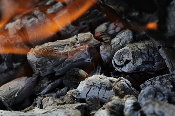 Fototapeta na wymiar Smoldered logs burned in vivid fire close up. Atmospheric background with flame of campfire. Unimaginable detailed image of bonfire from inside with copy space. Whirlwind of smoke and glowing embers.