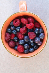 Orange ceramic cup with raspberries and blueberries on a table. Top view.