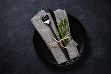 White plate, cutlery and napkin on black table top view. - obrazy, fototapety, plakaty