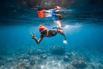 Happy freediver woman with New year cap glides underwater in blue sea. Christmas holidays concept