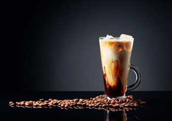 Ice coffee in frozen glass and coffee beans on a black reflective background.