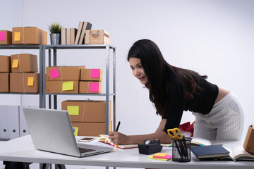 Beautiful lady checking order from laptop and writing on book.Prepare for packing,working...