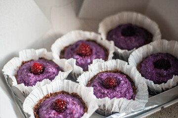 Box full of purple raw vegan cupcakes with raspberry on top