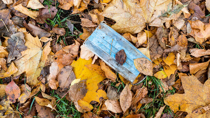 panoramic view of dirty used face mask in wet fallen leaves on lawn in city park in autumn