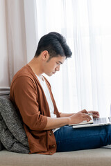 A young man working at home, sitting by the window with a laptop  (work from home)