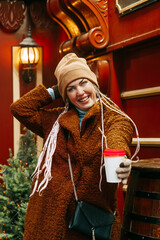 woman enjoying a hot beverage as she attends a Christmas street market or fair clasping a large mug
