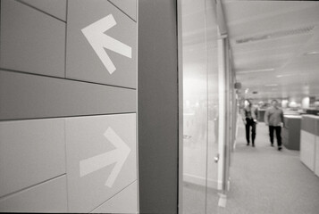 Close-up of arrow symbol on wall against colleagues walking in corridor at office