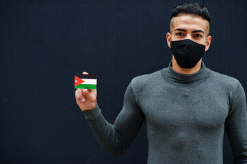 Middle eastern man in gray turtleneck and black face protect mask show Jordan flag isolated background.