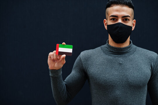 Middle Eastern Man In Gray Turtleneck And Black Face Protect Mask Show United Arab Emirates Flag Isolated Background.