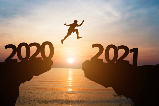 Happy new year 2021 and silhouette concept , Man jumping from 2020 to 2021 with beautiful orange sky and sea.