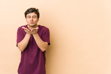 Young cool man folding lips and holding palms to send air kiss.