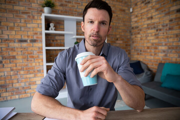 Portrait of man holding coffee cup while sitting on his desk