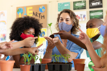 Female teacher wearing face mask showing plant pots to students in class