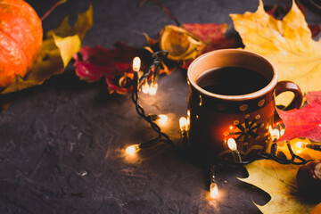 Cup of black coffee, autumn maple leaves and lights on dark background. Cozy autumn seasonal background.