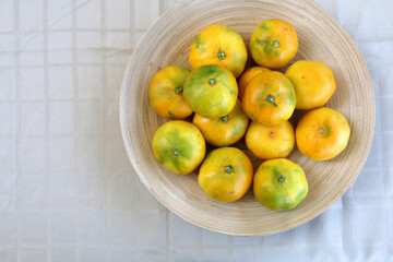 Wooden bowl full of tangerines on a table. Top view.
