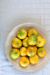 Wooden bowl full of tangerines on a table. Top view.