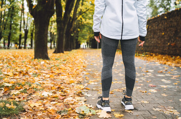 Young fit athletic woman wears modern running clothes standing on the footway before jogging in the autumnal city park. Active running people concept image.