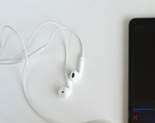 Headphones and part of a smartphone on a white background. Creative flat photo of a desktop with headphones and mobile phone, white background, copy space. View from above.