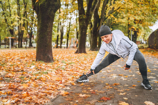 Fit athletic woman doing workout before jogging in the autumnal city park on the kids playground. Mid aged fitness female runner stretching legs while warming up. Active runners people concept image.