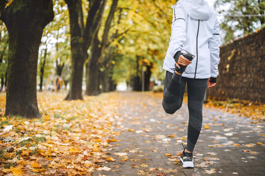 Fit athletic woman doing workout before jogging in the autumnal city park. Young fitness female runner stretching legs while warming up. Active running people concept image.