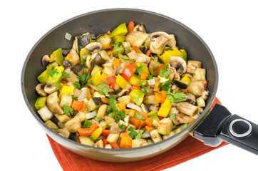 Frying pan with fried seasonal vegetables and mushrooms on white