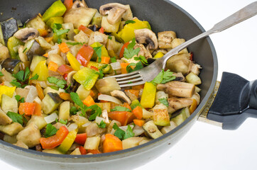 Frying pan with fried seasonal vegetables and mushrooms on white