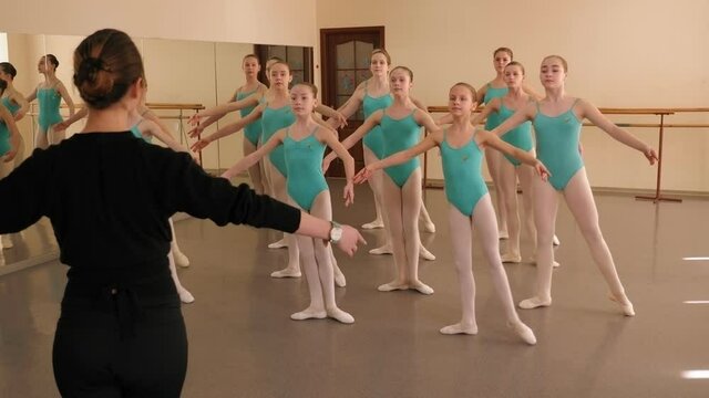A young female choreographer teaches classical ballet in a dance Studio for young ballerinas.