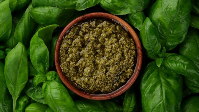 pesto alla genovese in wooden bowl and basil leaf around, rotating.  top view
