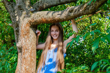 Young woman with long hair leans on tree branch in summer on a sunny day
