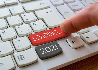 Finger about to press a keyboard key with the text 2021 loading. Year two thousand and twenty one...