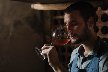 Young bearded man drinking wine from glass at cellar