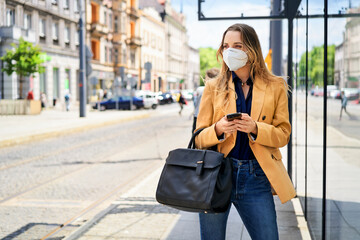 Woman wearing protective face mask while waiting at tram station during COVID-19