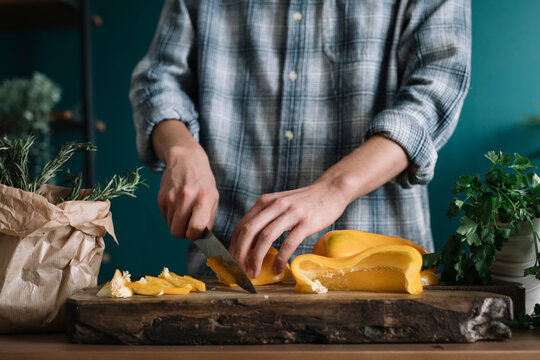 Hands of man cutting yellow bell pepper on board in kitchen
