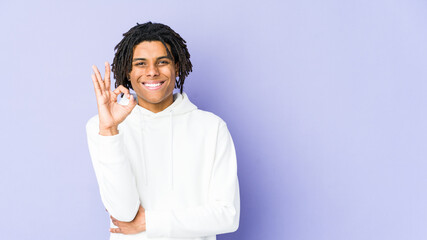 Young african american rasta man winks an eye and holds an okay gesture with hand.