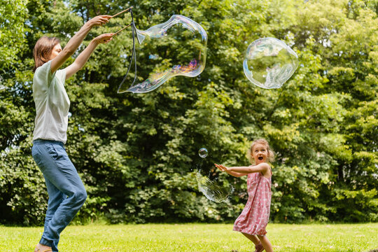 Happy daughter exploding bubble with mother at park